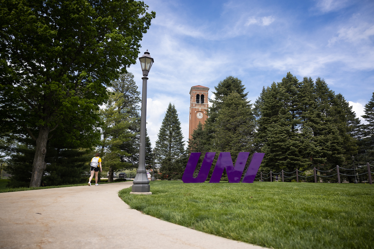 Person walking by UNI sign with campanile in the background